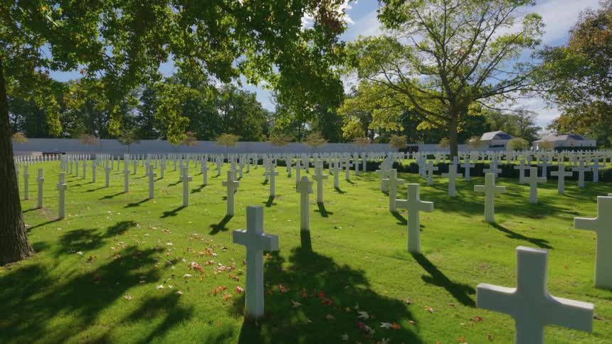 A slow, serene pullback shot reveals the countless white crosses of a military cemetery on a bright, sunny day