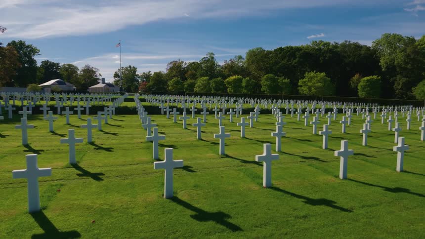 A wide, steady shot of a military cemetery with endless rows of white crosses on a sunny day