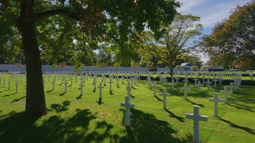 A slow zoom reveals endless rows of white cross headstones at a sun-dappled military cemetery