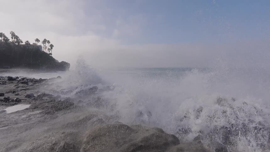 A massive ocean wave explodes in a dramatic slow-motion splash against a rocky shoreline