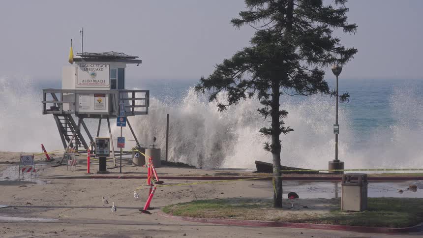 A powerful ocean wave crashes in dramatic slow motion next to a lifeguard tower at a closed-off Aliso Beach in Laguna Beach, California