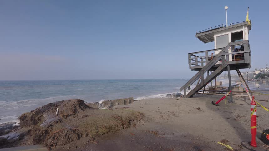 A huge ocean wave crashes in slow motion on a sandy beach next to an empty lifeguard tower