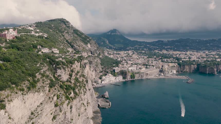 A stunning aerial view shows the picturesque coastal town of Sorrento, Italy, nestled along dramatic cliffs with a boat gliding across the beautiful blue sea