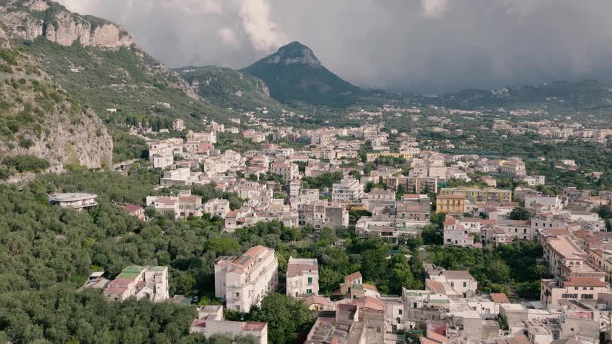 Slow aerial view flying over the historic town of Sorrento, Italy, revealing the classic architecture nestled amongst the mountainside forests
