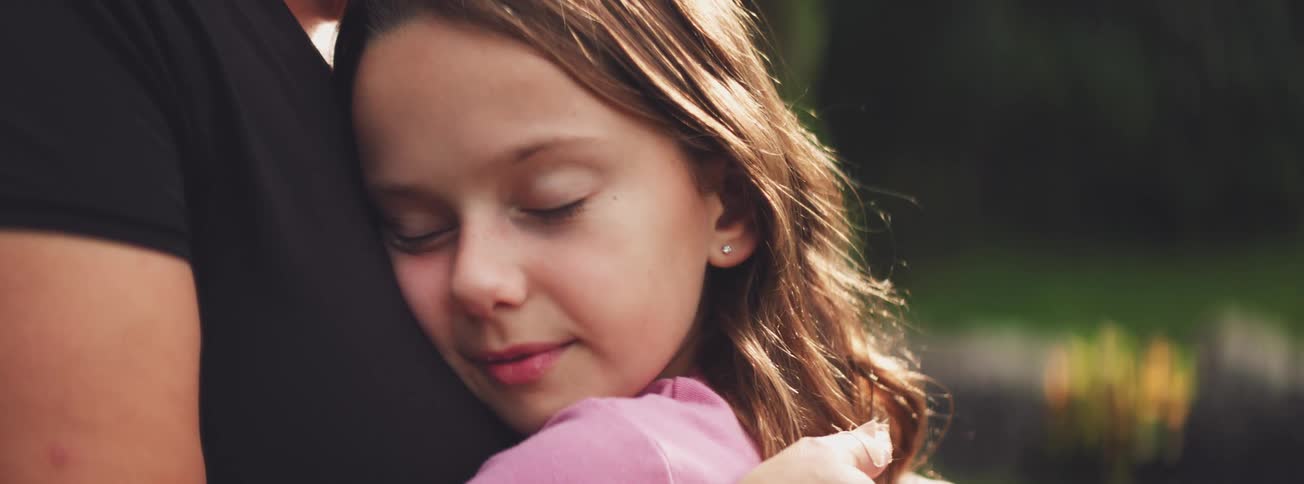 An adorable young girl gently closes her eyes as she receives a warm and loving hug from her parent