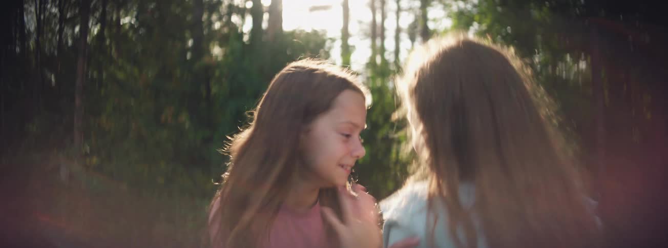 Two joyful sisters laugh and playfully hug each other while enjoying the sunny weather in a beautiful park