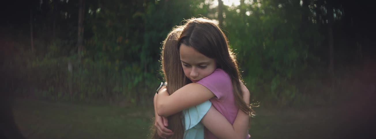 A young girl finds comfort and solace as she shares a long, loving hug with her sister outdoors at sunset