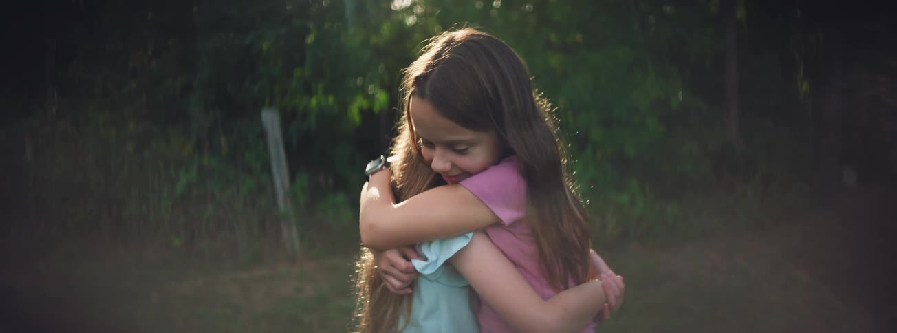 Two young sisters share a heartfelt hug in a sun-drenched field at golden hour