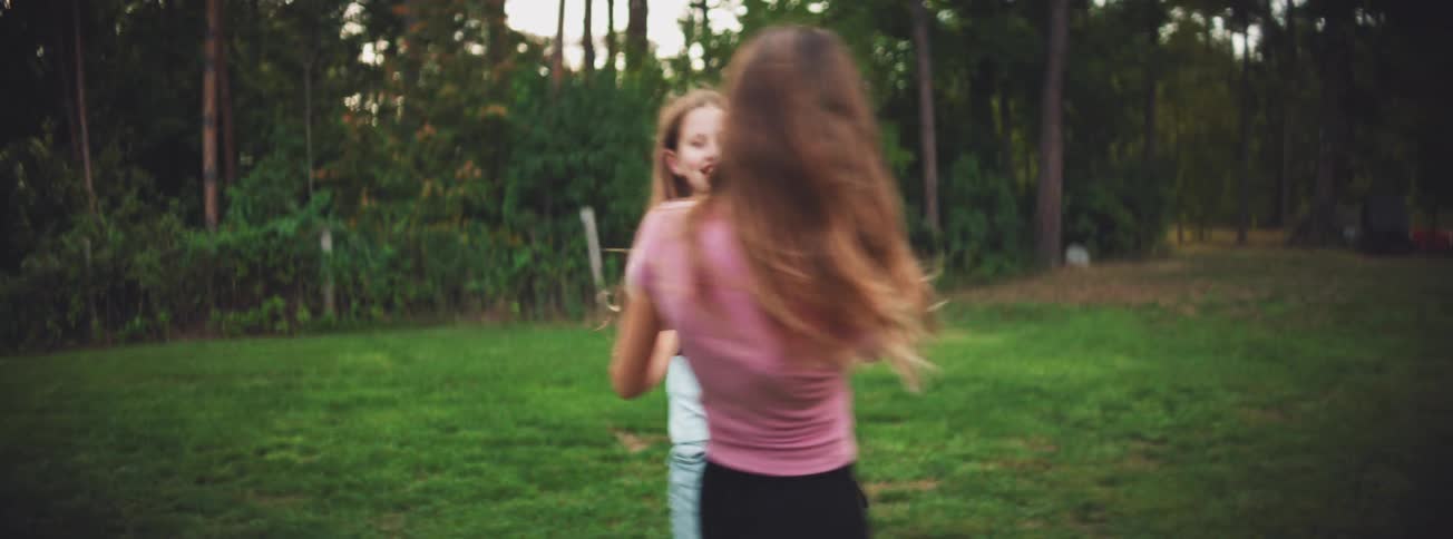 Carefree childhood moments as two girls spin together on a green lawn in slow motion