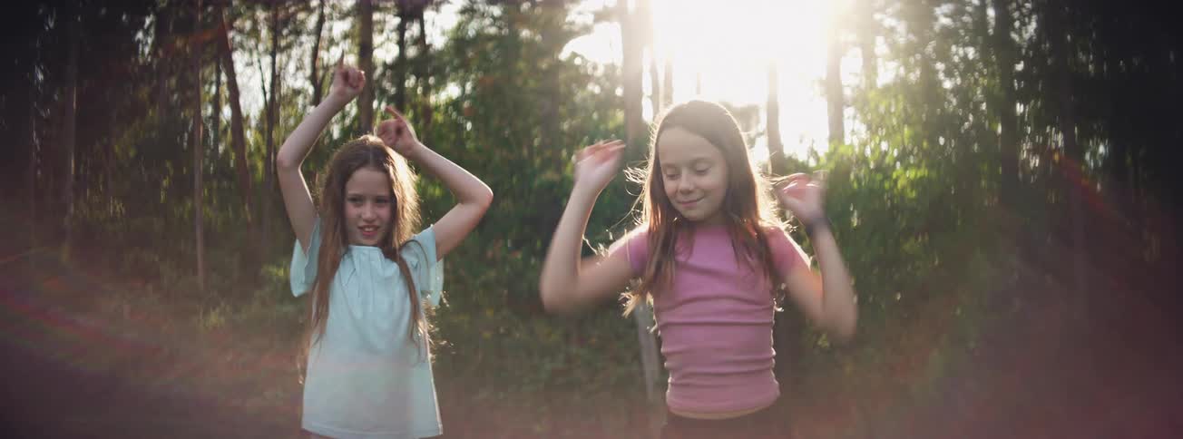 Two happy young girls energetically dance and jump together outdoors with golden hour backlighting