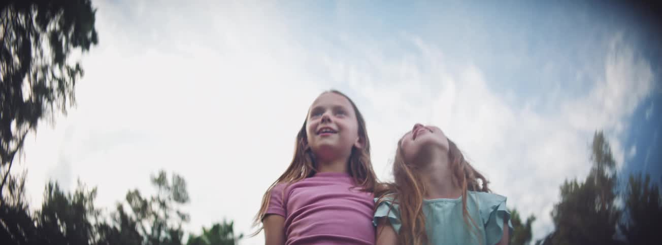A low-angle slow-motion shot of two young girl friends looking up with wonder and joy while playing together outside
