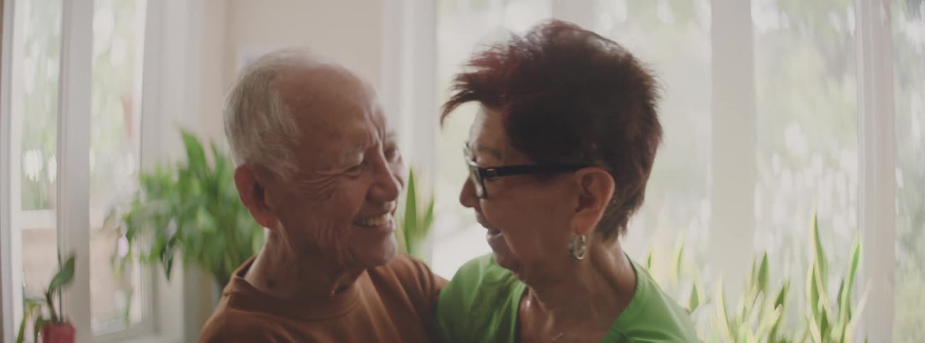 A happy elderly couple shares a tender and loving moment, smiling as the husband whispers in his wife's ear