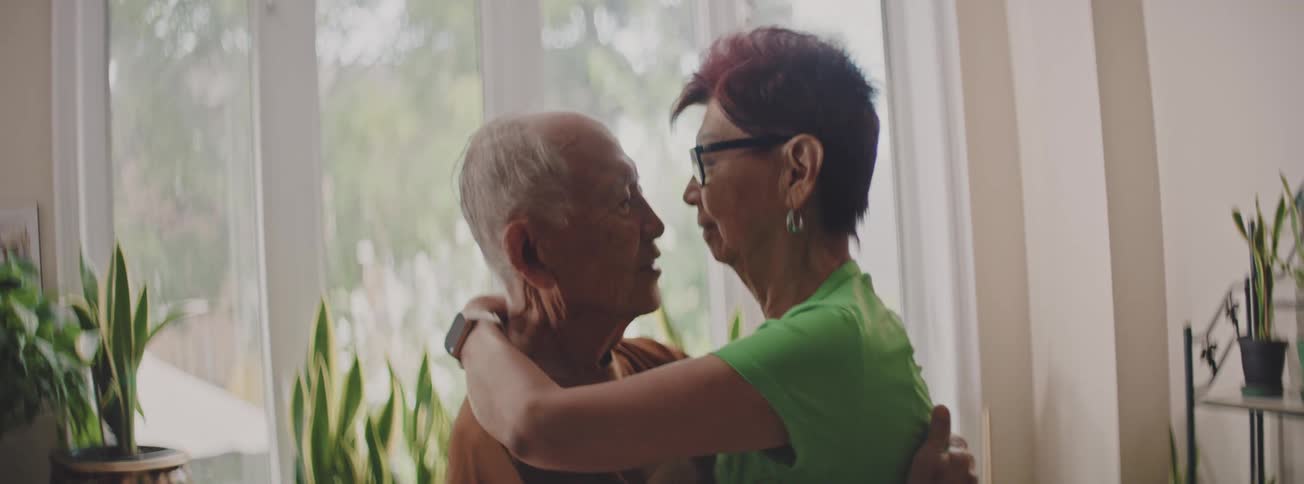 A loving senior couple hugs and kisses each other tenderly by a window