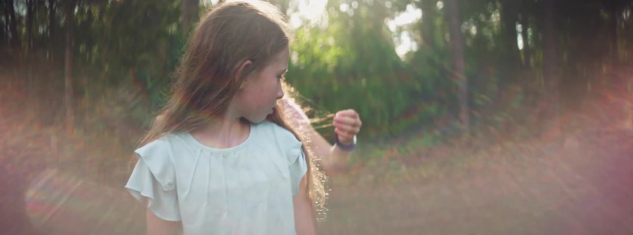 Two young girls share a moment of surprise and laughter after one pulls a small bug from the other's hair while playing outside