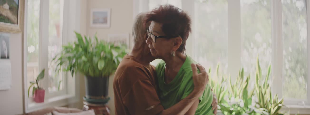 An affectionate elderly Asian couple embraces and sways gently while slow dancing in their sunlit home