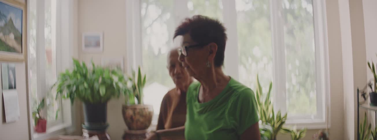 A daughter and her elderly father share a sweet dance together in their living room surrounded by plants