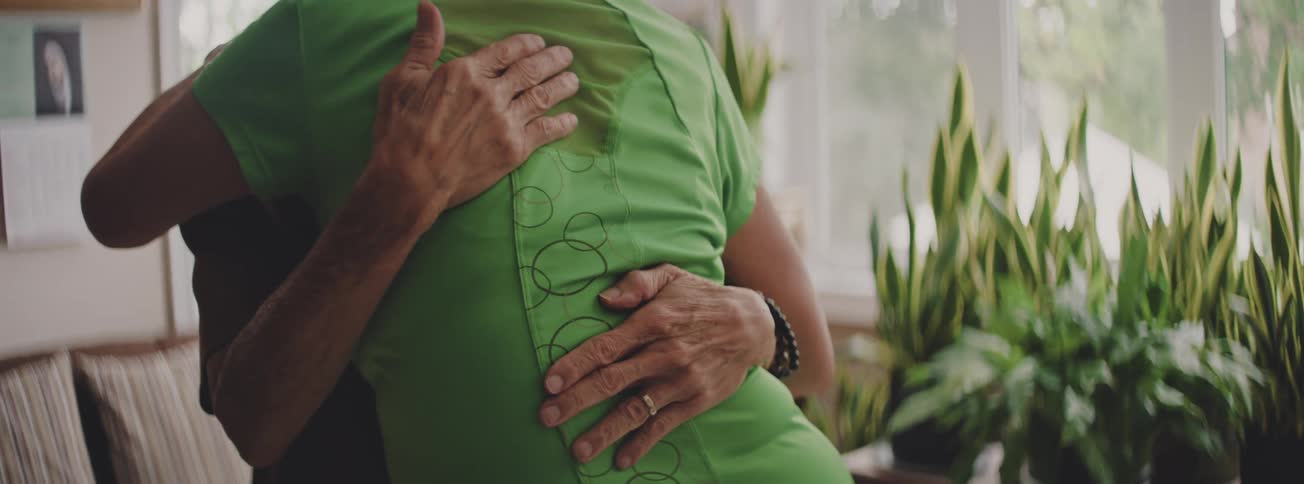A close-up of a senior person's hands gently patting another person's back during a comforting hug indoors