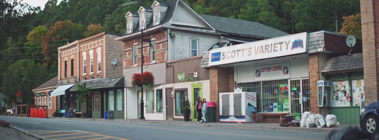 An establishing shot of a main street in a quaint small town as people walk and a car drives by
