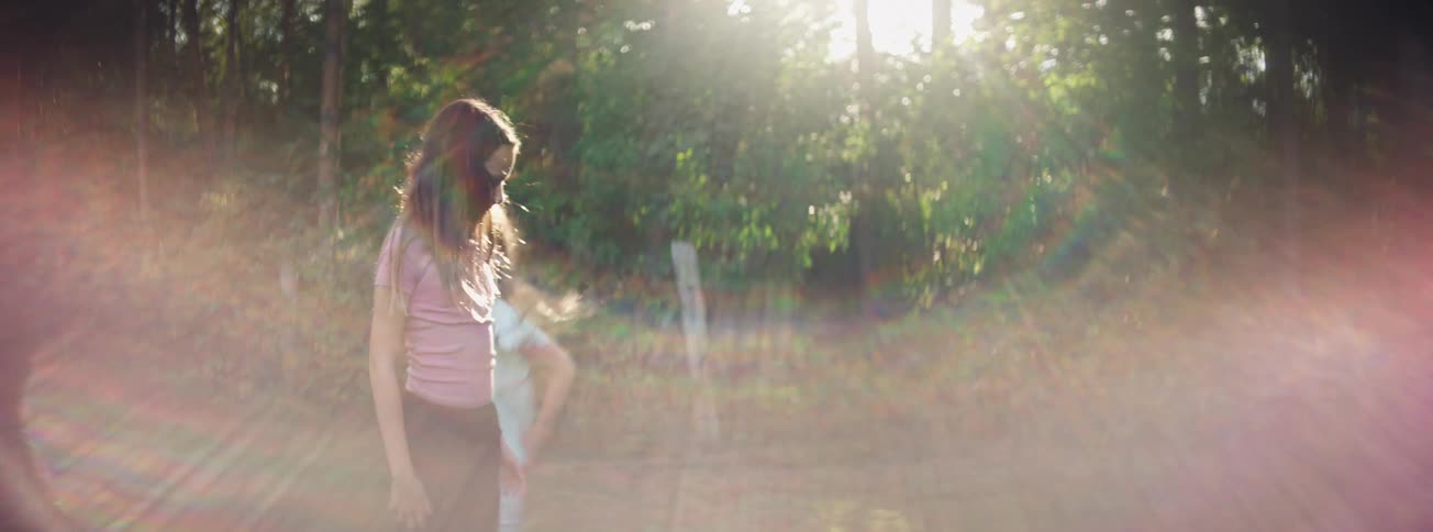 Two happy young girls playfully dance and chase each other in a sunlit forest clearing in slow motion