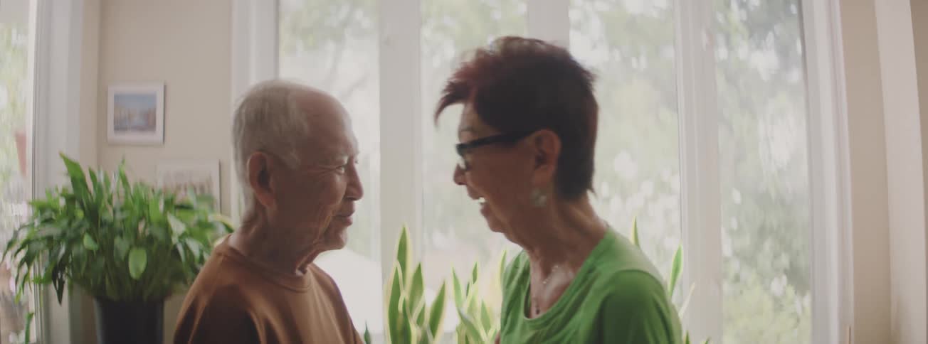 A happy senior couple shares a joyful laugh and a warm embrace by a bright window at home