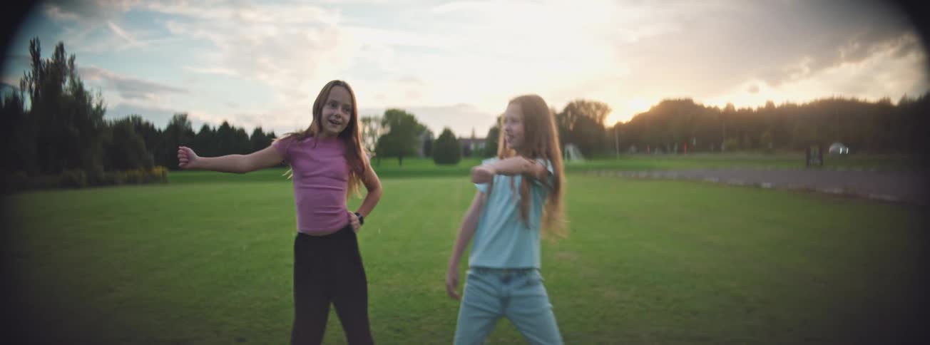 Slow motion shot of two carefree young girls dancing and laughing in a park as the sun sets