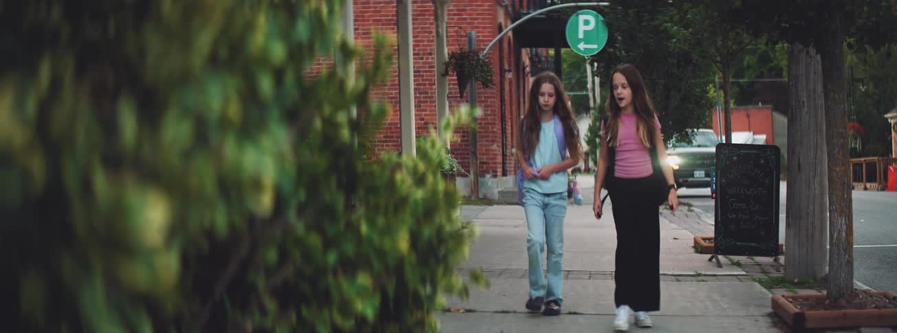 Two young schoolgirl friends walk and talk together on the sidewalk as they head home in a quaint town