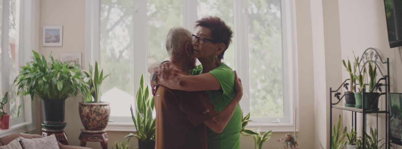 An affectionate senior couple slow dances and shares a loving hug in their sunlit living room
