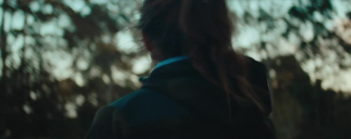 Slow-motion follow shot of a woman with a ponytail walking outdoors at sunset with beautiful golden bokeh