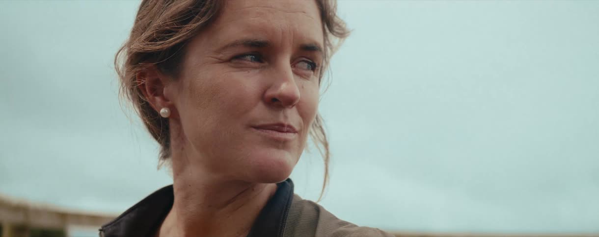 A close-up slow-motion shot captures a pensive woman with braided hair turning with a gentle smile as a white horse comes into view