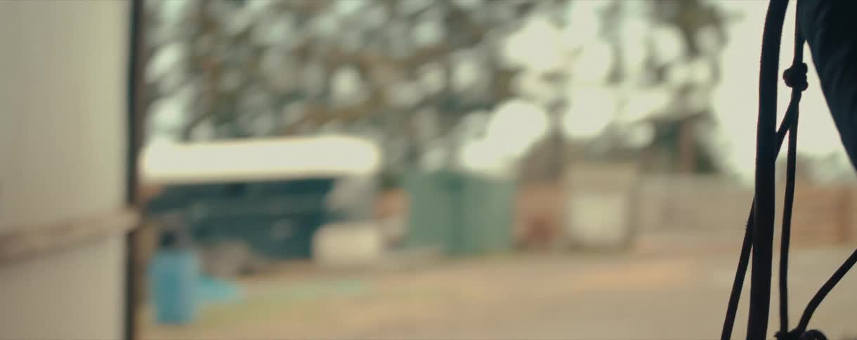 A woman carries a lead rope out of a dark stable in slow motion, preparing to ride her horse