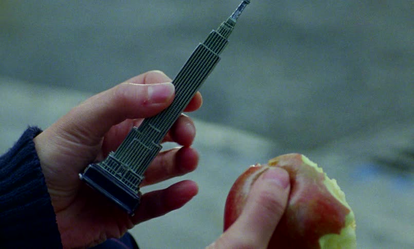 Close up of a person's hands holding a souvenir replica of the Empire State Building and a half-eaten apple