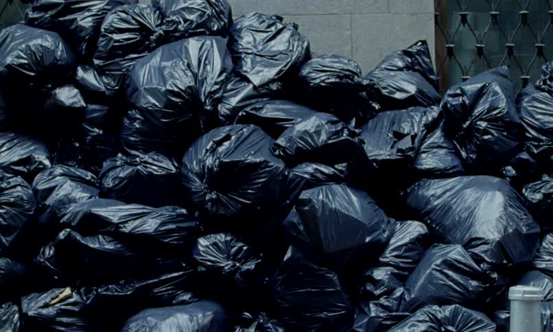 A large pile of black garbage bags stacked high against a wall in an urban setting