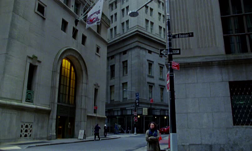 A woman bundled in a long coat and scarf walks across a quiet street corner in New York City's financial district