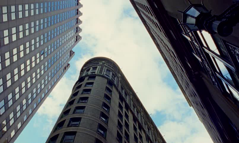 A worm's-eye view of towering city buildings reaching towards a cloudy blue sky