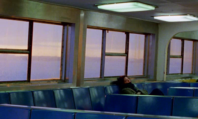 A solitary woman sleeps on an empty commuter ferry as the sun rises over the water