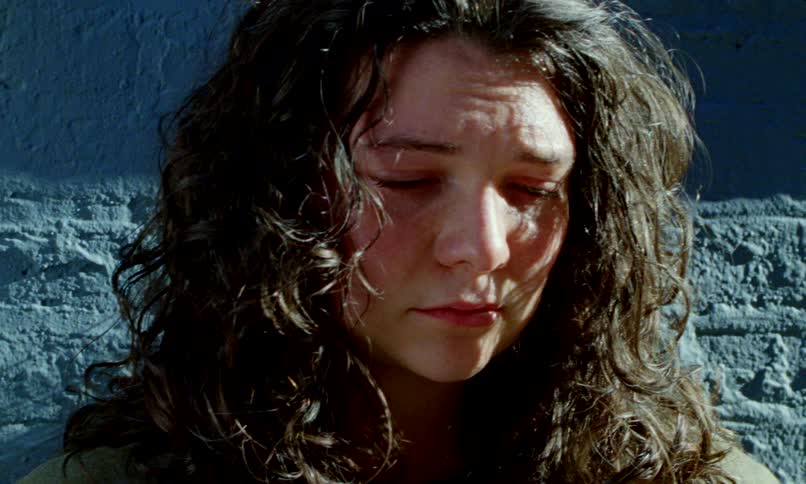 A close-up of a distraught woman with long curly hair crying with anguish while leaning against a brick wall