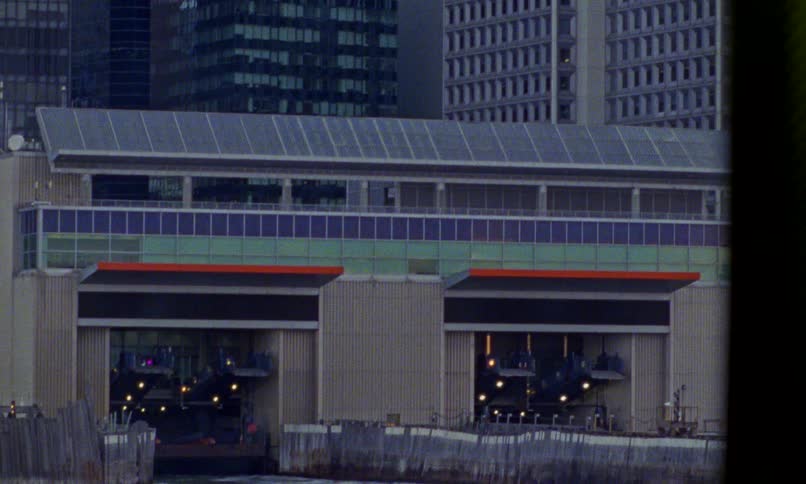 A slow tilt down from the modern skyscrapers of New York City reveals the Whitehall Ferry Terminal at the waterfront