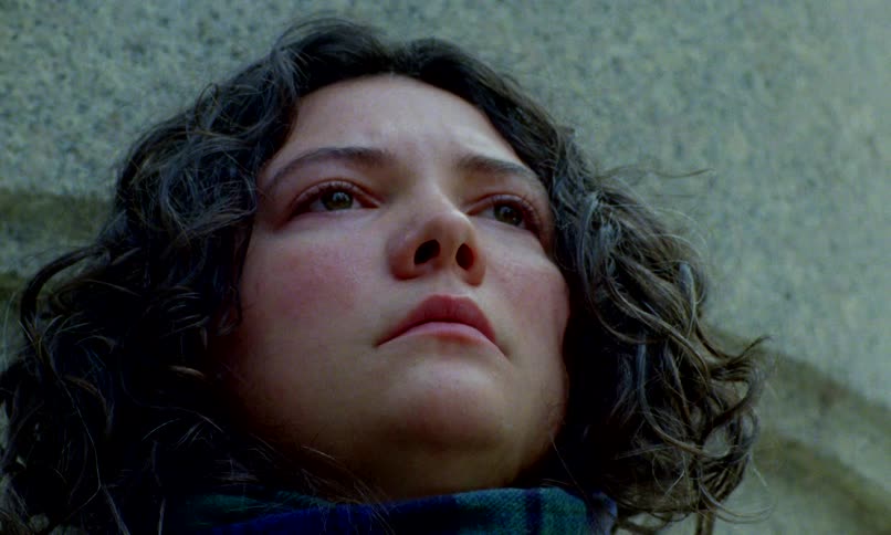 An emotional close-up of a young woman with curly dark hair, her sorrowful eyes looking up in deep contemplation
