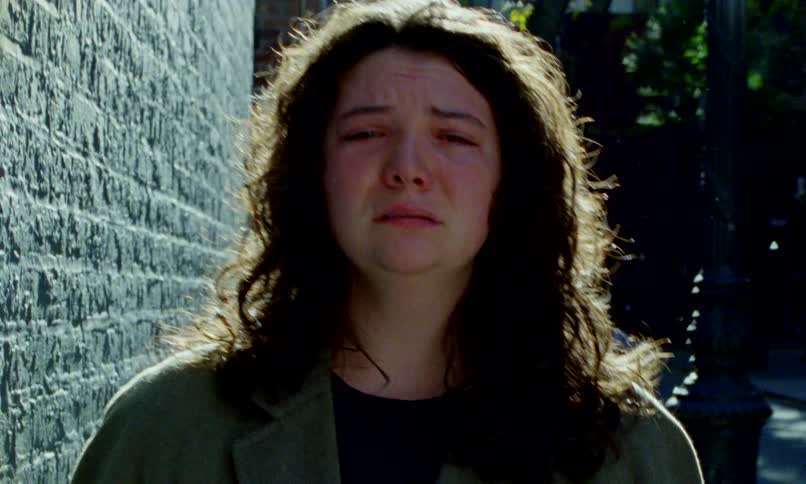 An emotional close-up of a young woman crying against a brick wall in a city alley, her face showing deep despair and sadness