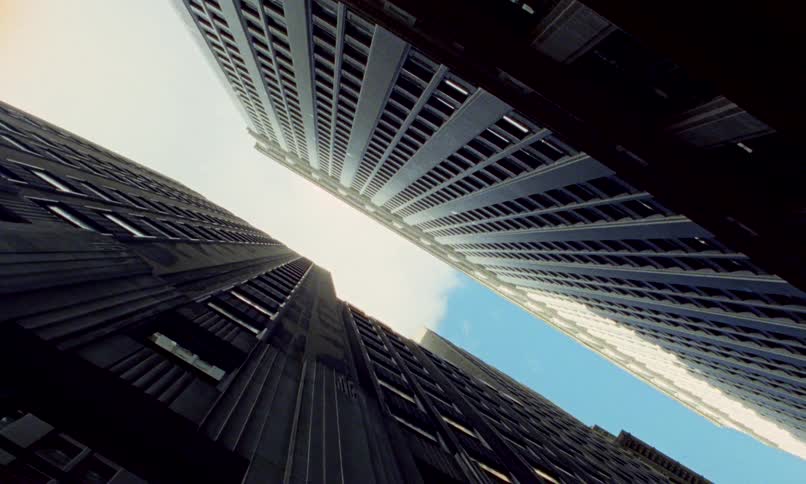 A dramatic low-angle shot slowly pushes in between two towering skyscrapers towards a patch of blue sky