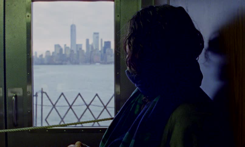 A mysterious woman holds a sharp tool while riding a ferry, pensively looking out at the New York City skyline