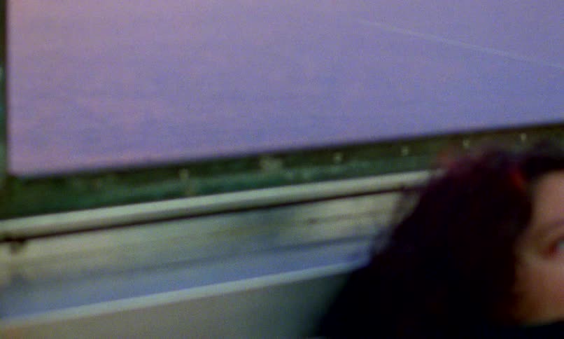 From a hazy seascape at twilight, the camera reveals a pensive woman bundled in a scarf, traveling by train