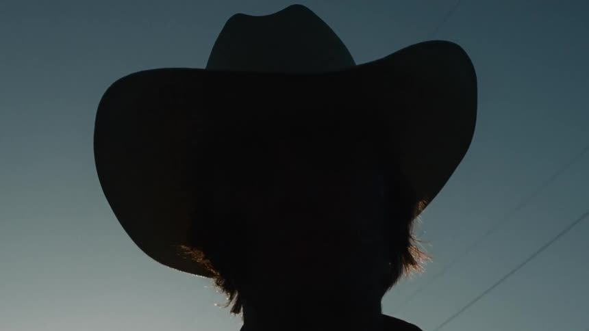 A dramatic low angle close up shot of a cowboy's silhouette against a clear sky at sunset