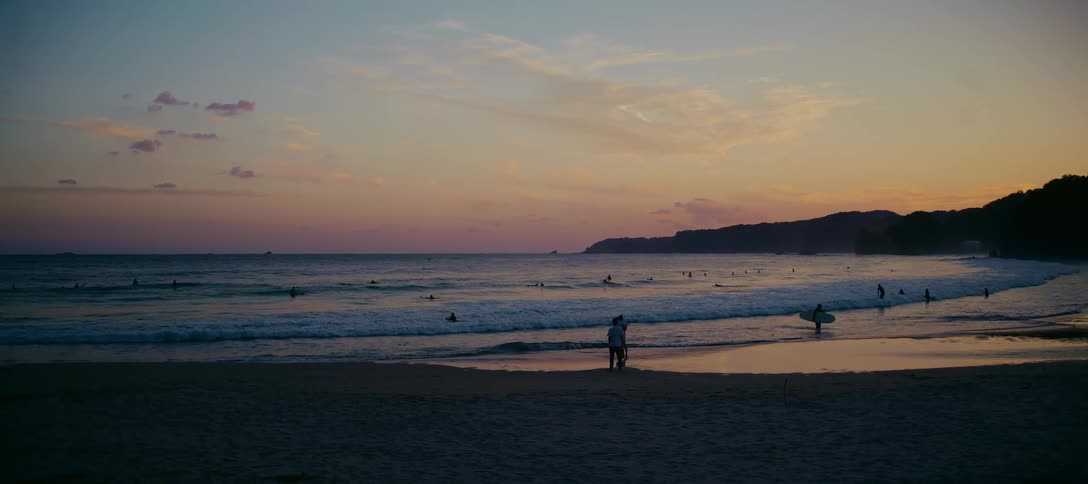 Surfers enjoying the last waves of the day as a couple watches from the beach during a beautiful sunset