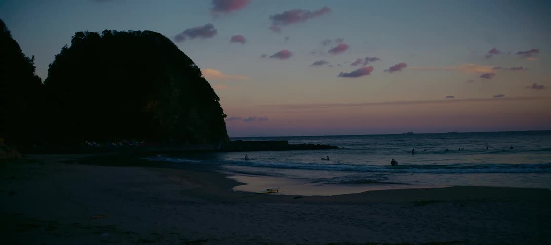 A serene beach at dusk with gentle waves and surfers enjoying the colorful twilight sky