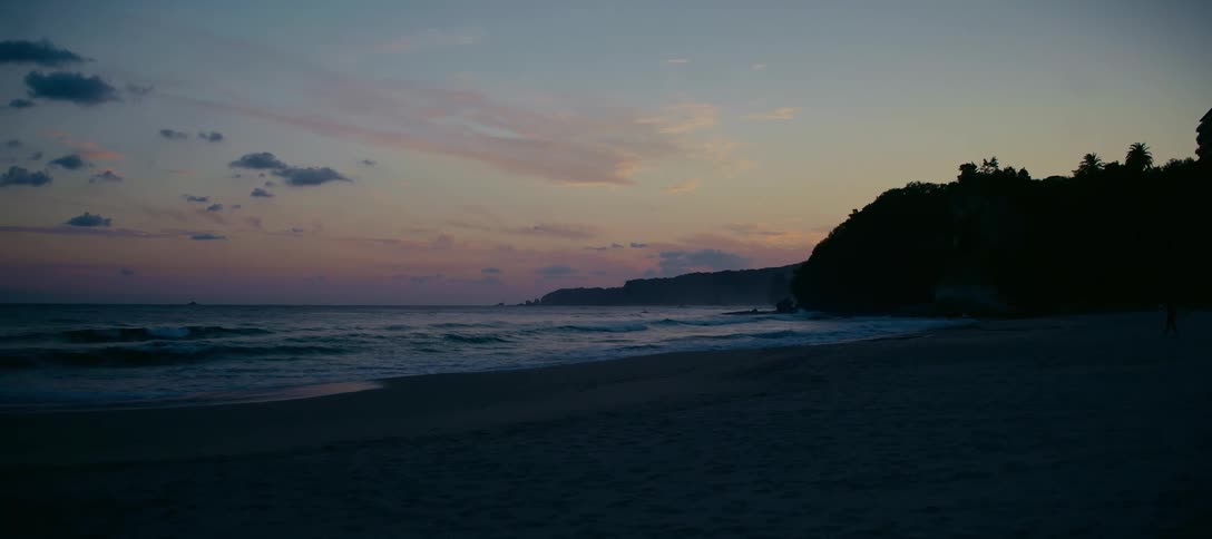 A tranquil coastal scene at dusk shows gentle waves lapping the shore under a pastel sky