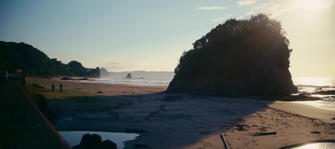Wide shot of two people walking on a scenic, rocky beach during a beautiful sunrise