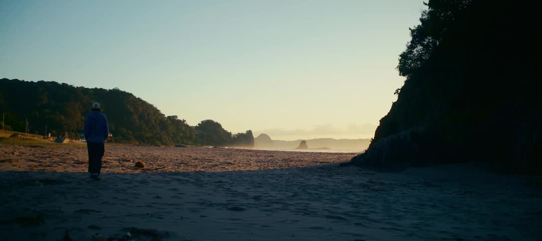 A solitary figure walks out onto a vast, tranquil beach at dawn to enjoy the serene coastal view