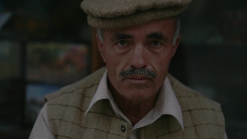 A man in a hat looks to the side and blinks