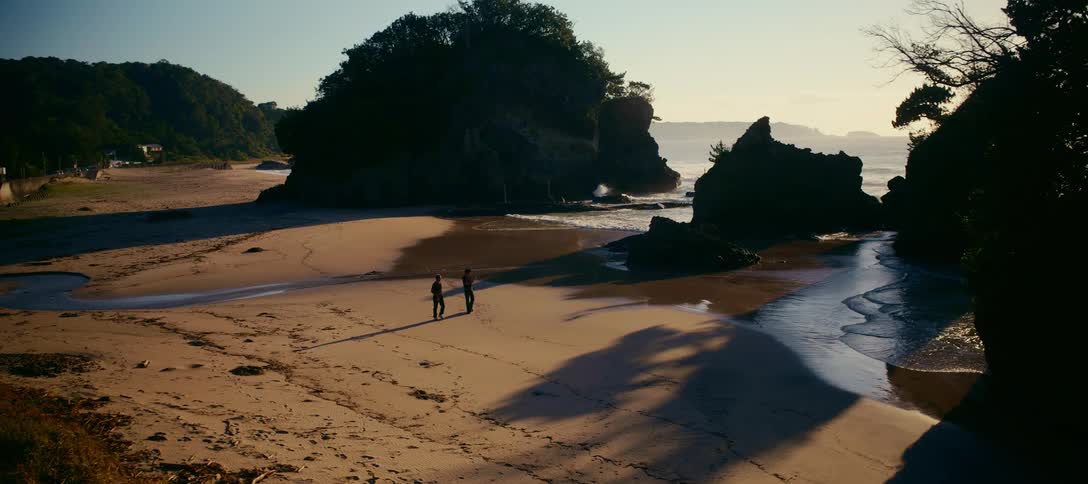 Two people walk along a beautiful, expansive beach with large rock formations during a golden sunrise